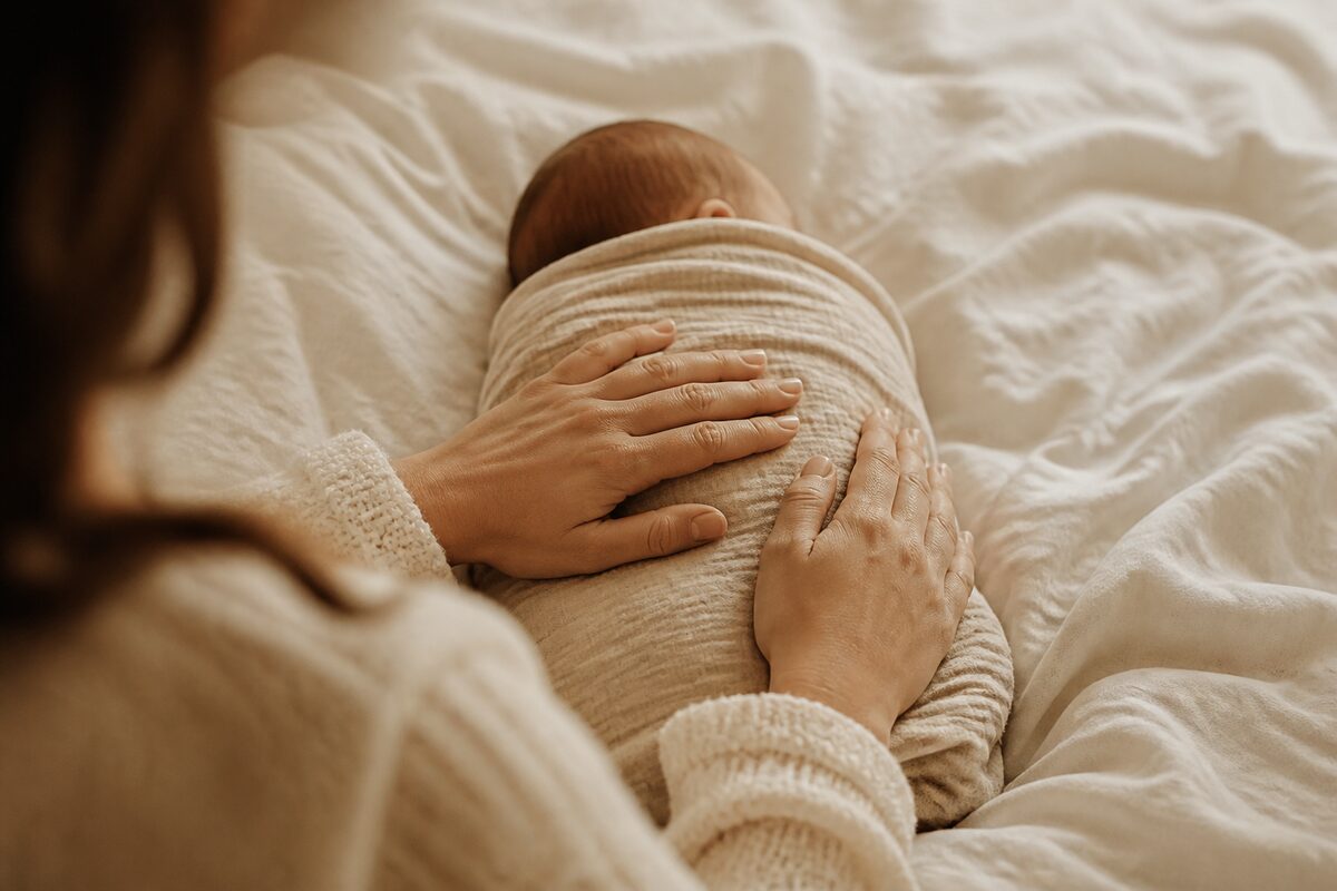 A mother's hands resting on her swaddled newborn